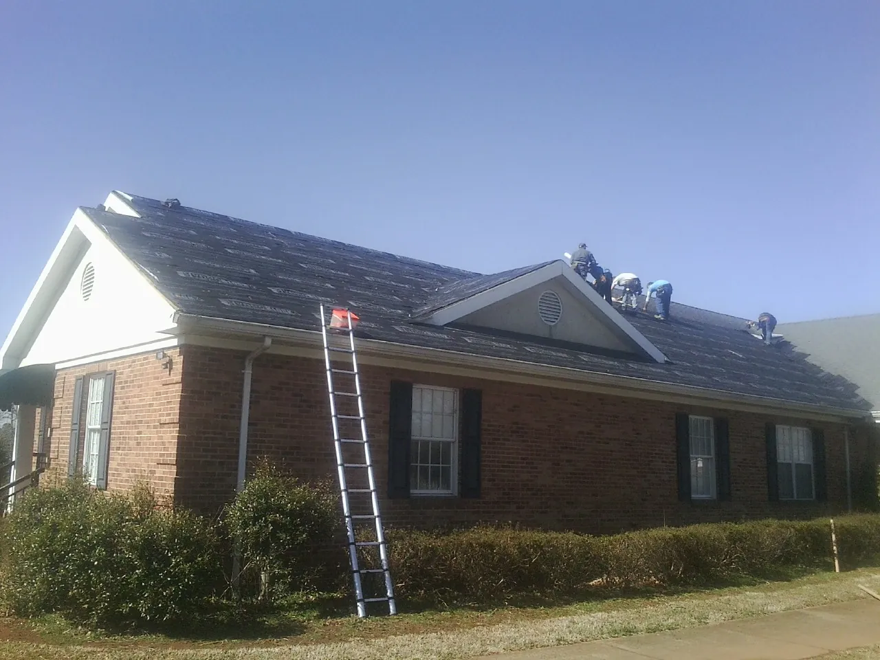Crew tearing shingles off a brick ranch roof with a ladder set — Metal Roof Repair work by our crew in Hamden