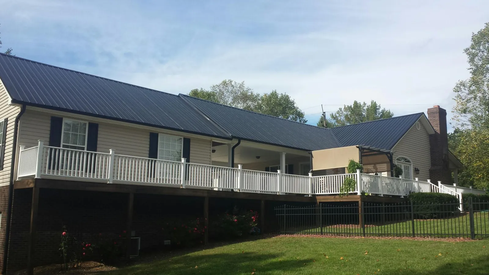 Black metal roof above a long white railed deck on a hillside home in Hamden