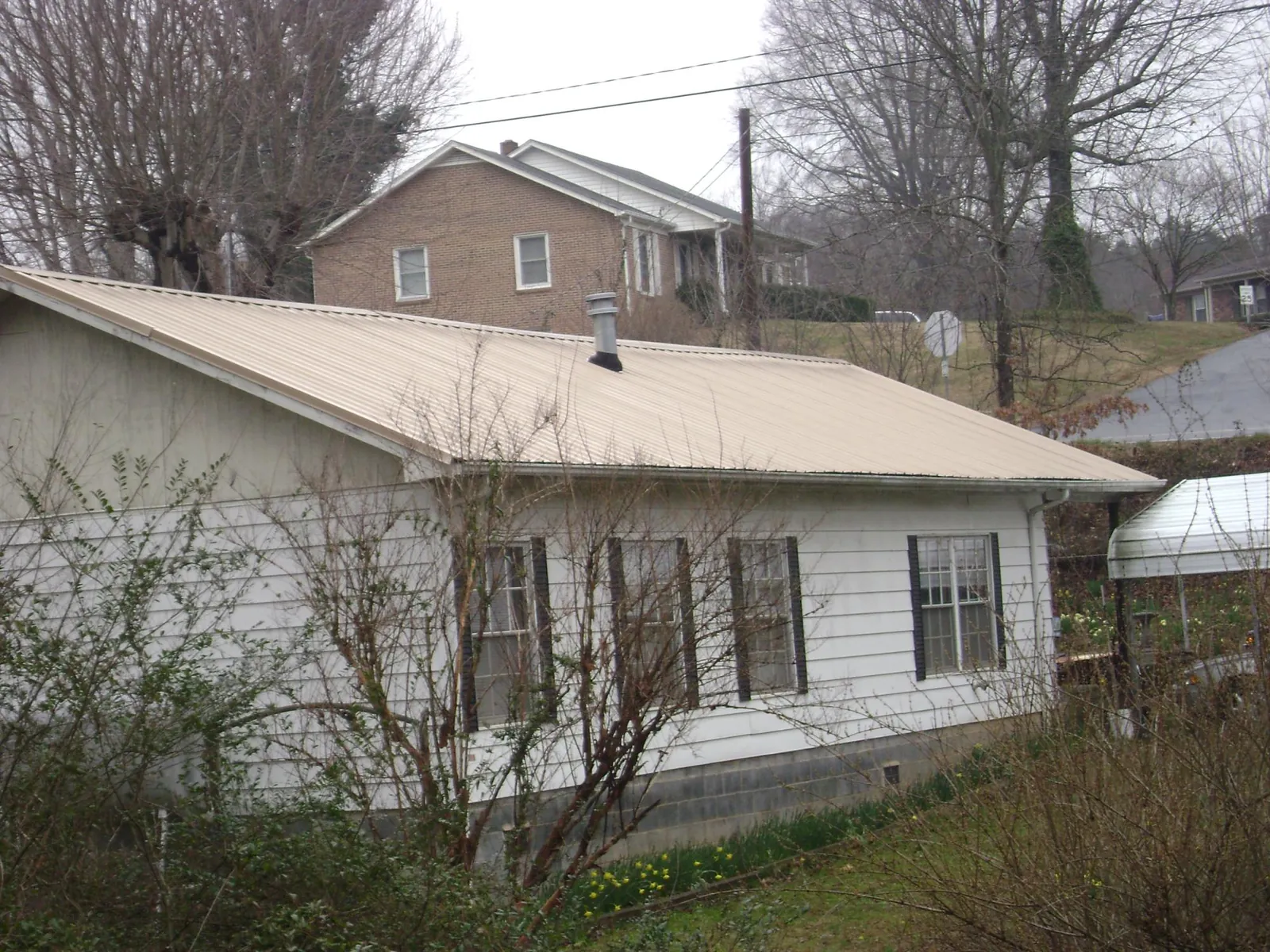 Tan metal roof on a white sided house set into a hillside — Commercial Roofing by Roofing Brothers in Hamden